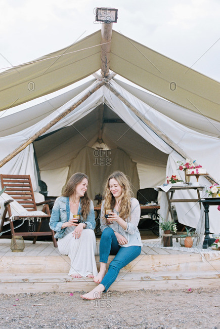 Two women sitting outside a large tent laughing and having a glass of wine