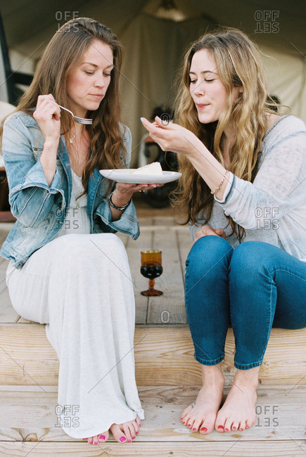 Two women sitting outdoors, sharing cake and a glass of wine