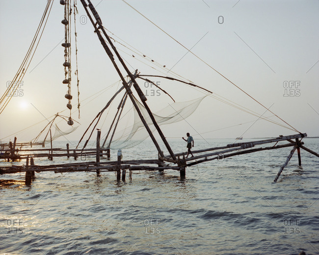 Mid distance view of man walking on commercial fishing net at sea during sunset