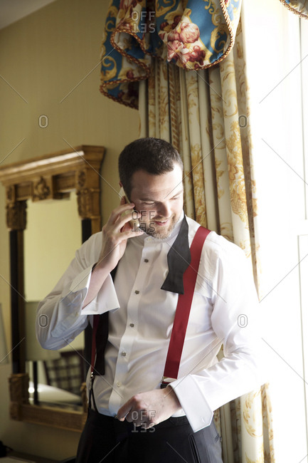 A groom talks on the phone while preparing for his wedding