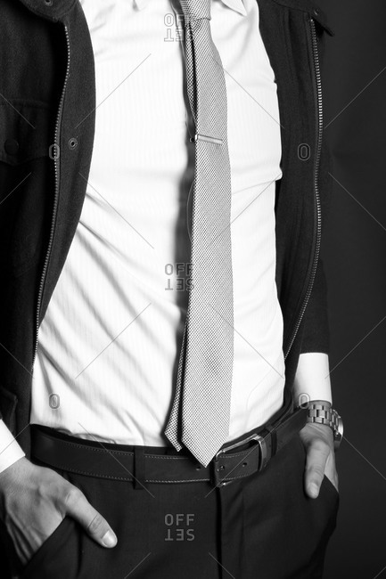 Fashion shot of man wearing a zip jacket with white shirt, tie, and black pants