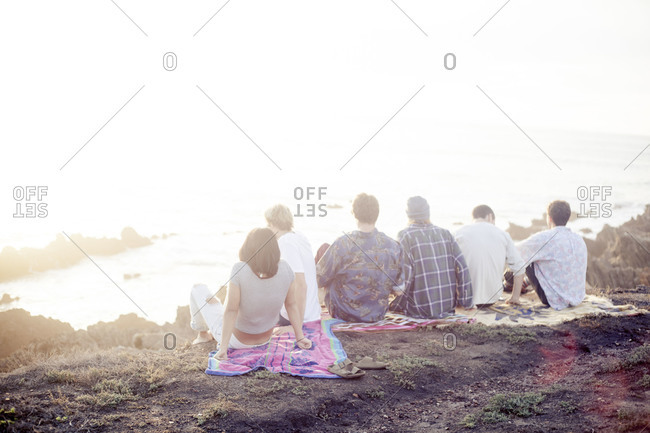 Group of friends sitting on a blanket on cliff overlooking the ocean