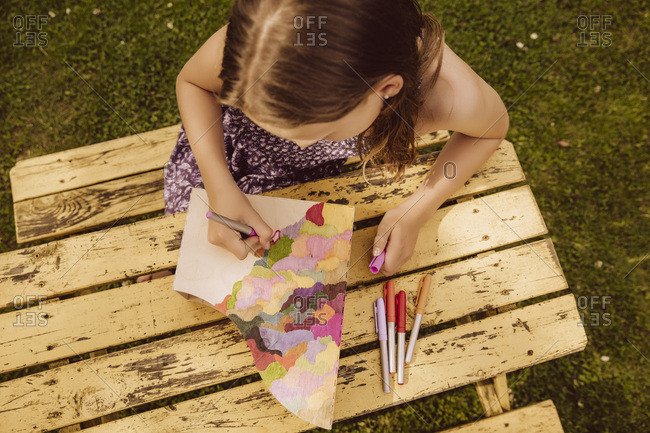 Girl drawing on a wooden magazine file in garden