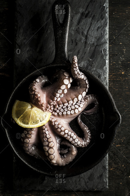 Overhead view of fresh octopus in a skillet with lemon slice