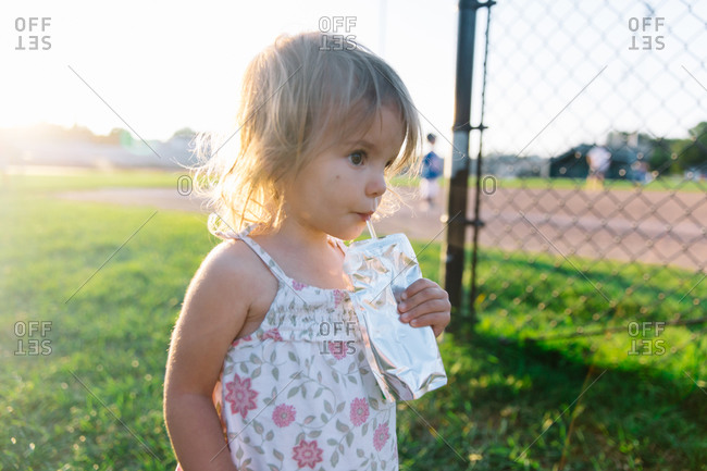 Toddler girl drinking from a juice pouch at a baseball field