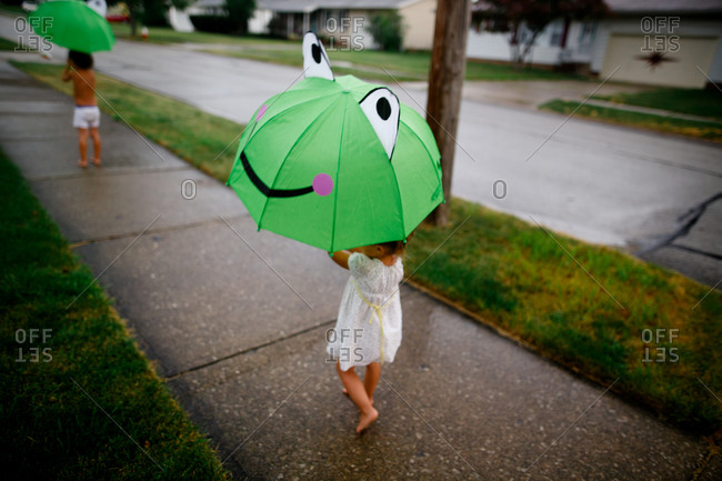 Kids walking on sidewalk in rain with frog umbrellas
