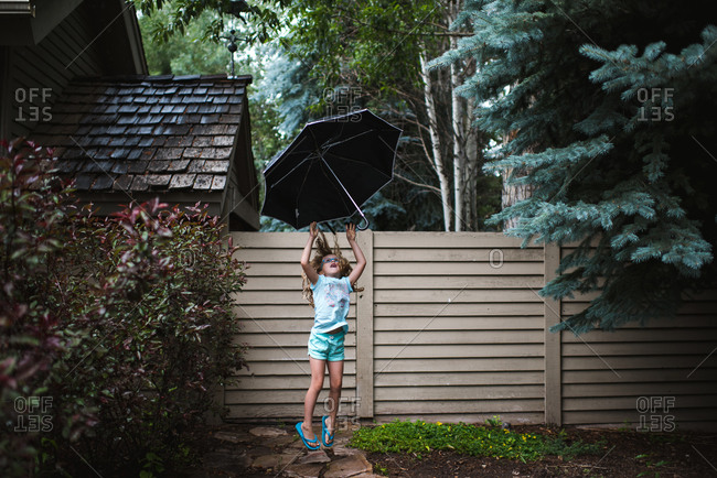 A girl jumps after a blowing umbrella