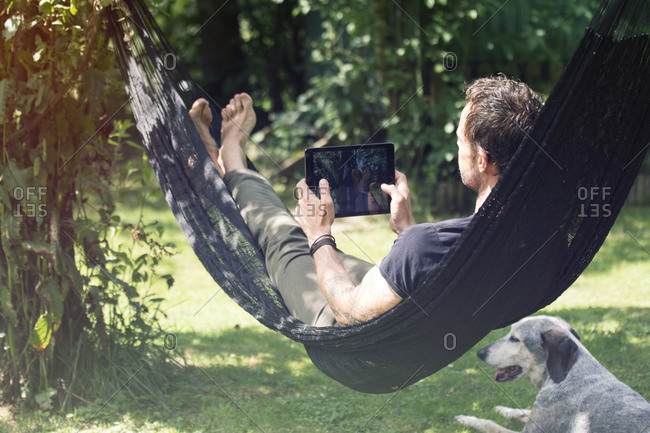 Relaxed man lying in hammock with digital tablet and dog beside him