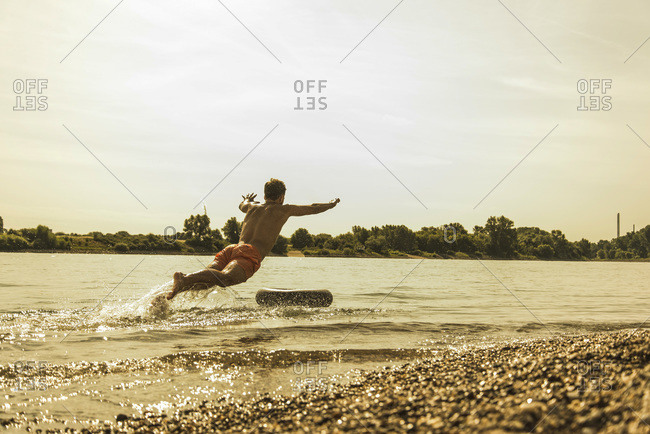 Young man jumping in river with inner tube
