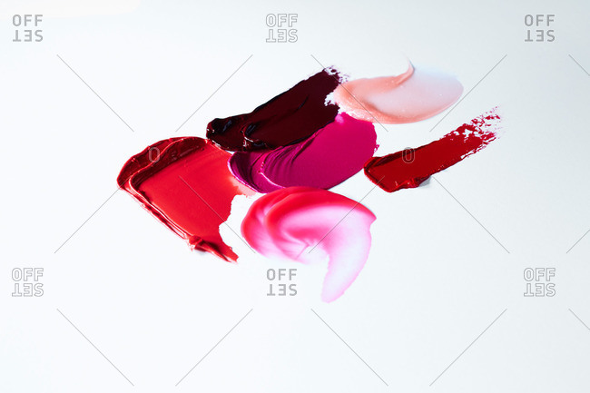Smeared red and pink lipsticks and lip gloss on white surface