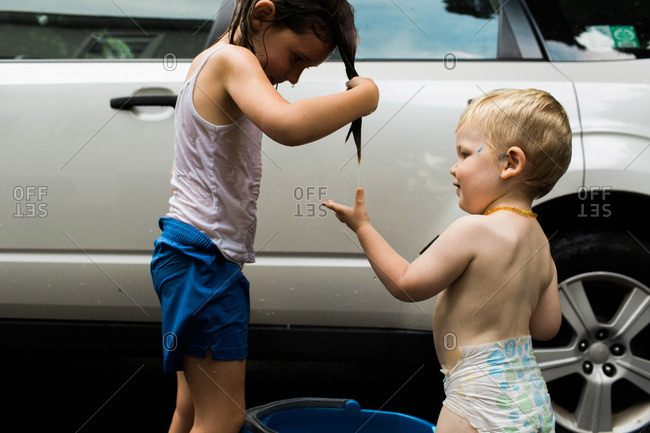 A girl drips water from her hair while washing a car