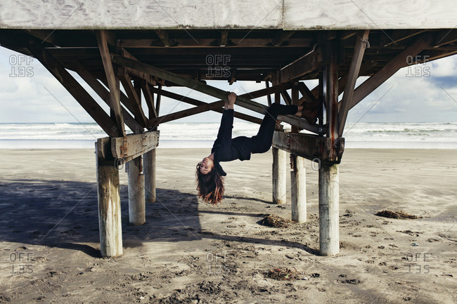 Woman hanging upside down from the support beams of a lifeguard tower