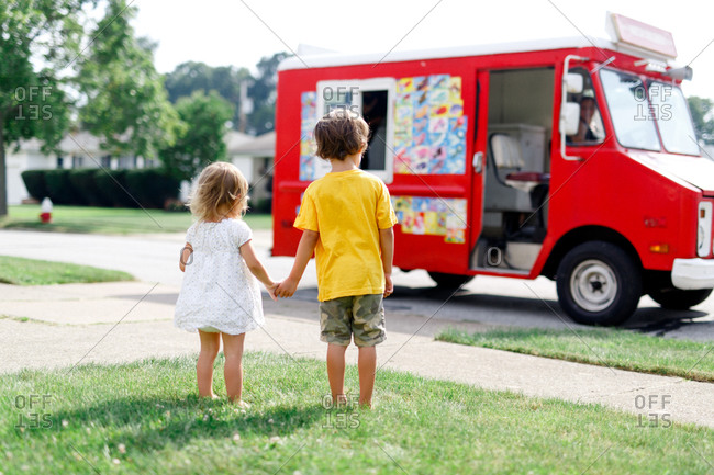 Two young siblings holding hands waiting for ice cream truck