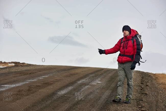 A man hitchhiking for a ride on empty road in Iceland