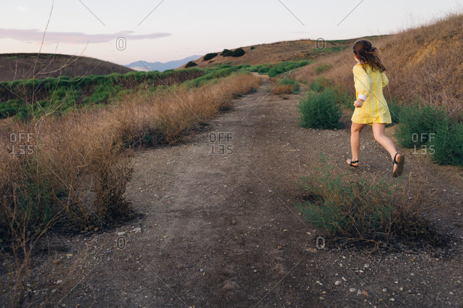 Young girl in vintage yellow dress running on path on rural hillside