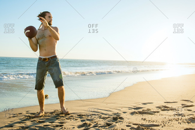 Young man throws a football at the beach