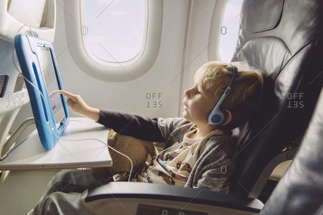 Little boy sitting on an airplane watching something on digital tablet