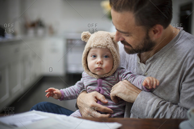 A baby in a bear hat being  held by her father who gazes at her lovingly