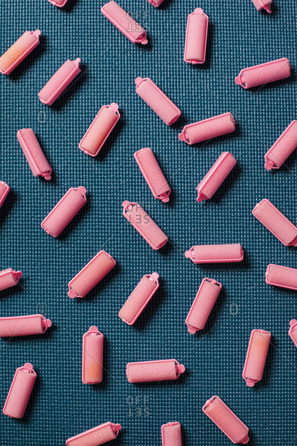 Pink foam hair rollers are scattered across a turquoise background