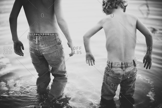 Two boys in jeans wading in water