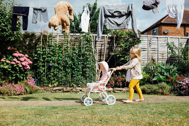 Little girl pushing a doll stroller beneath a clothesline