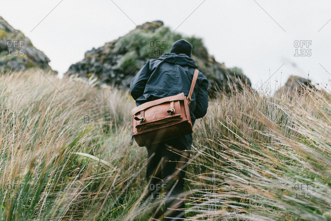 Man with a leather satchel hiking through tall grass
