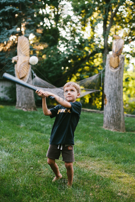 Boy swinging bat to hit a wiffle ball in backyard