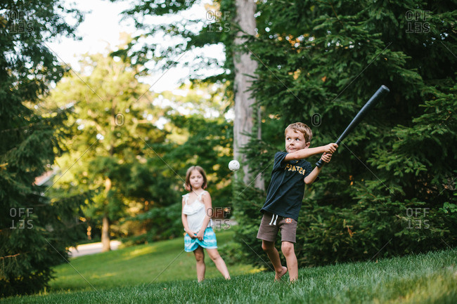 Boy and girl playing wiffle ball in backyard