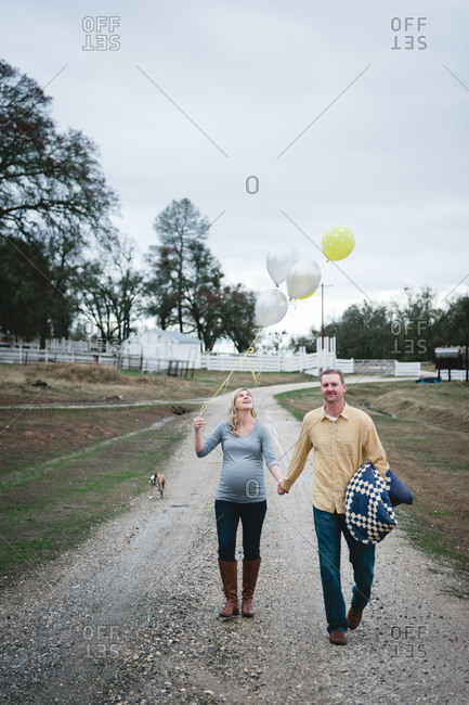 A pregnant woman walks down a  gravel path with her husband and dog