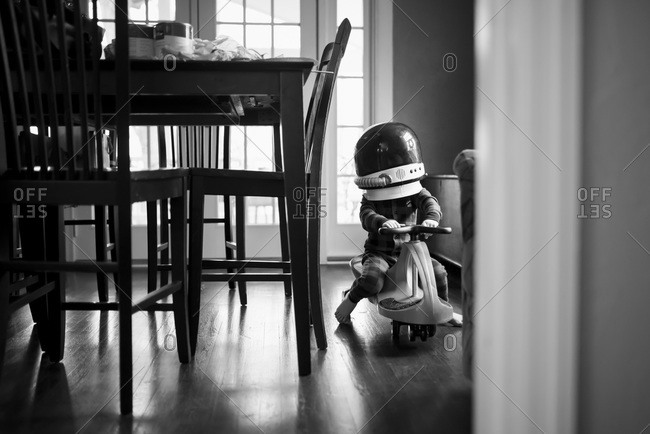 Child rides scooter indoors wearing astronaut helmet