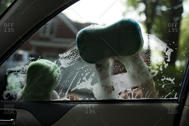 Two boys wash car window with soapy sponges