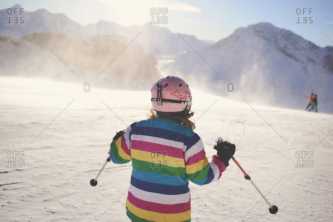 Girl in striped jacket and pink helmet skiing down slope