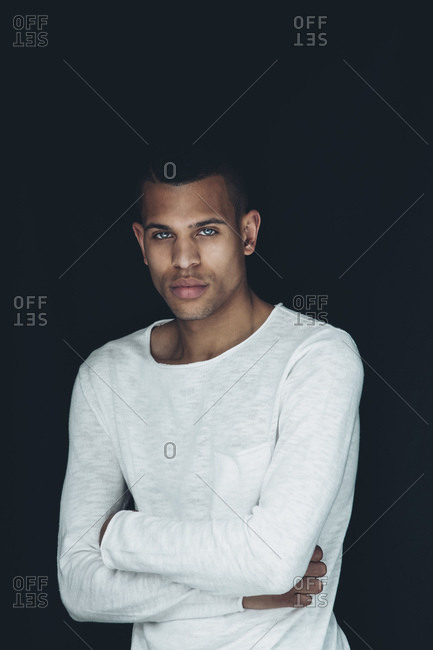 Portrait of young man with crossed arms wearing white sweatshirt in front of black background