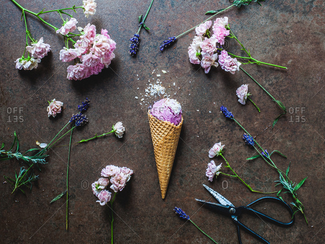Berry ice cream cone on rustic stone surface surrounded by fresh cut flowers
