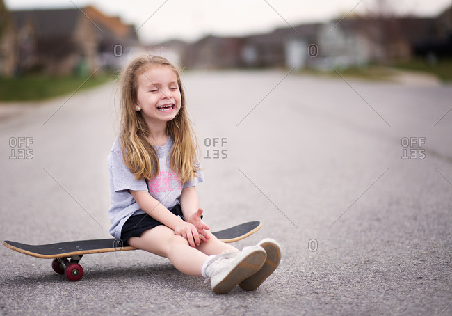 Smiling girl sitting on skateboard in middle of street