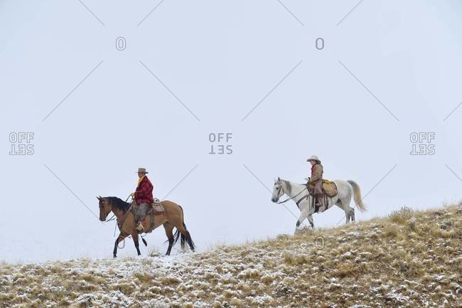 Cowboy with young cowboy riding along horizon with snow, Rocky Mountains, Wyoming, USA