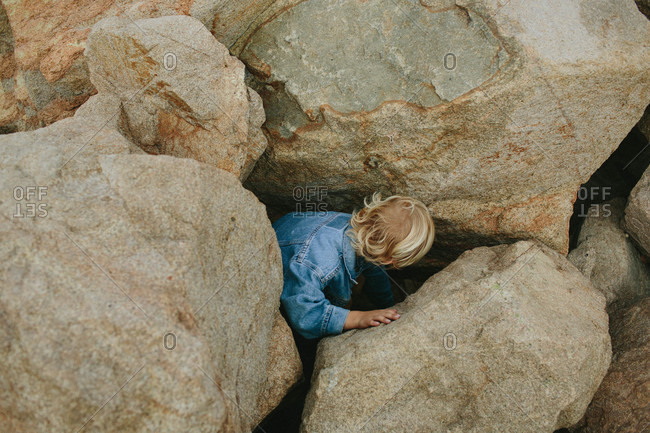 Little boy crouching between large rocks