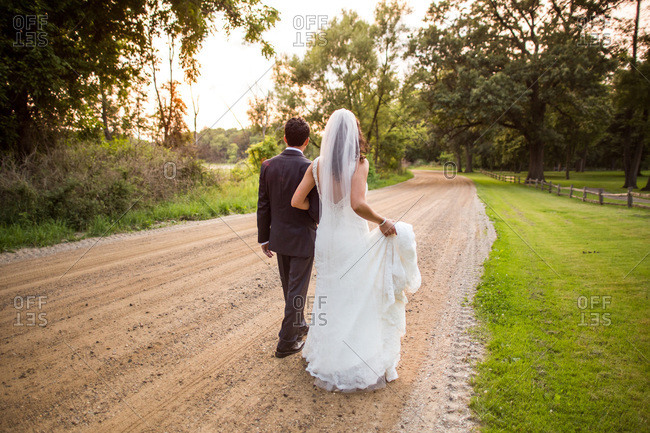 Back view of bride and groom walking along country dirt road at dusk