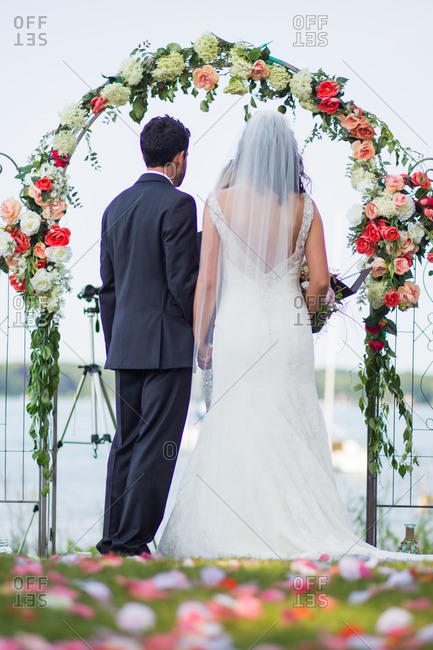 Back view of couple during wedding ceremony under arch decorated with roses and hydrangea