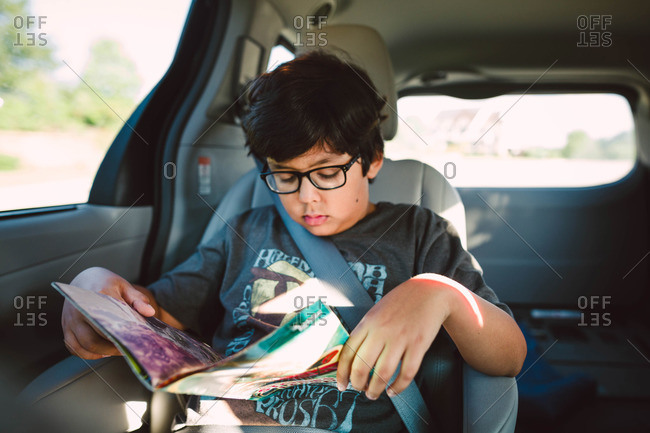 A boy reads a magazine in the back of a minivan