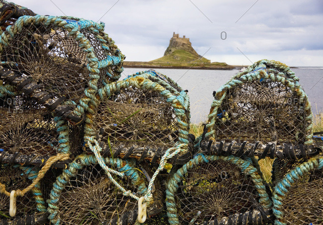 Traps piled on the water's edge with lindisfarne castle in the distance, Lindisfarne, Northumberland, England