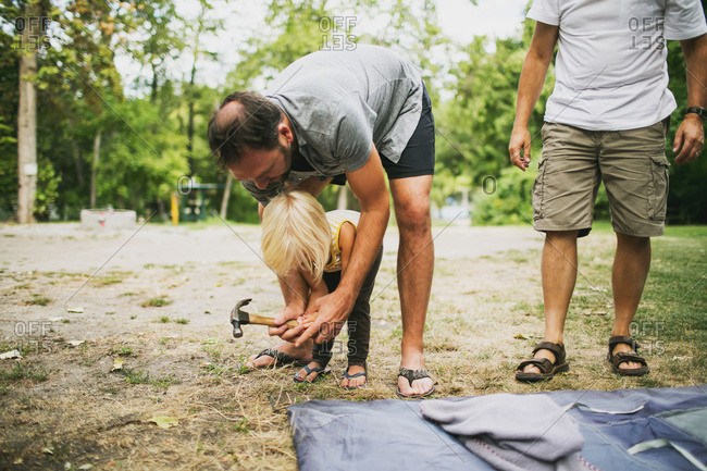 A father and young daughter work together to hammer in tent pegs at a campsite, Peachland, British Columbia, Canada