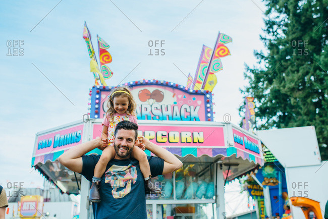 Girl riding on her dad\'s shoulders at a fair