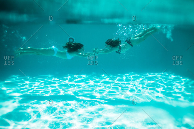 Two girls hold hands underwater in a pool