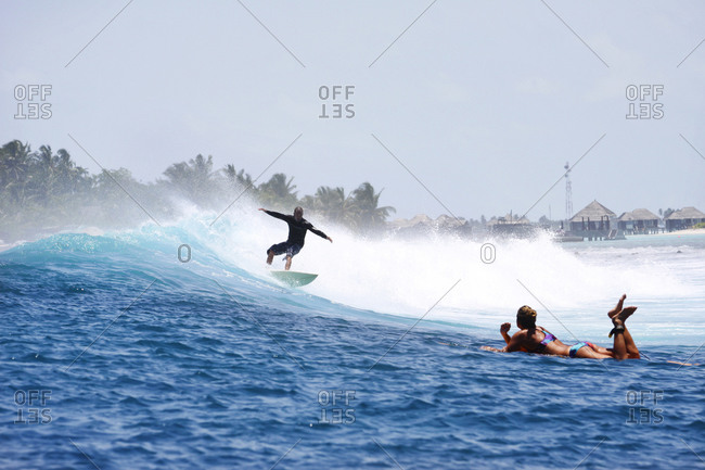 Man surfing while woman lying on her surfboard watching him, South Male Atoll, Maldives
