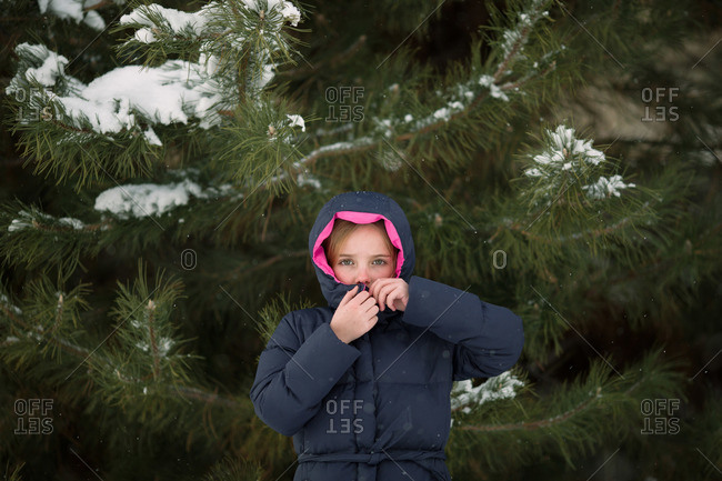 Girl zipping up jacket by fir tree in winter