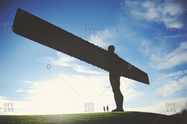 Two girls holding hands below the Angel of the North statue near Gateshead, England
