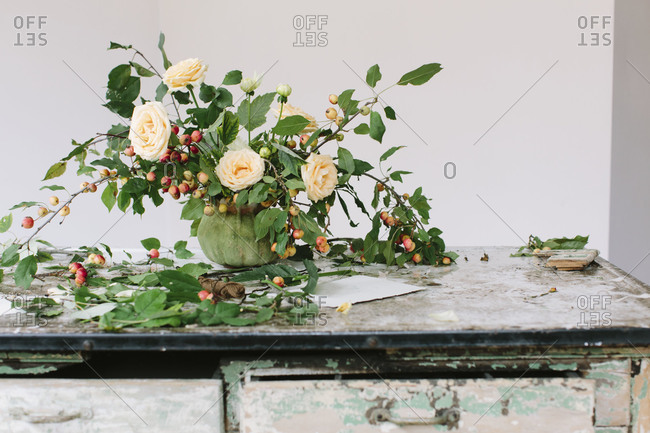 Elegantly rustic flower arrangement of apple branches and peach roses in vintage pot on rustic workbench