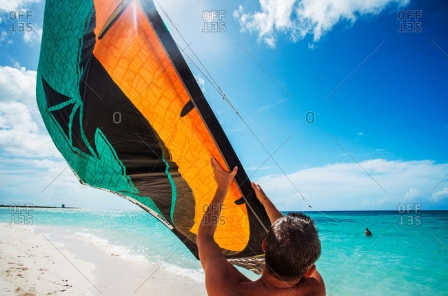 Kite boarder launches from white sand beach into the Caribbean water