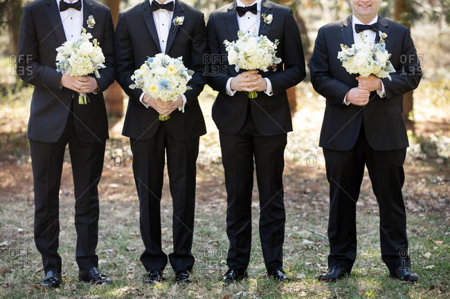 Neck down shot of four groomsmen in tuxedos holding bouquets of flowers
